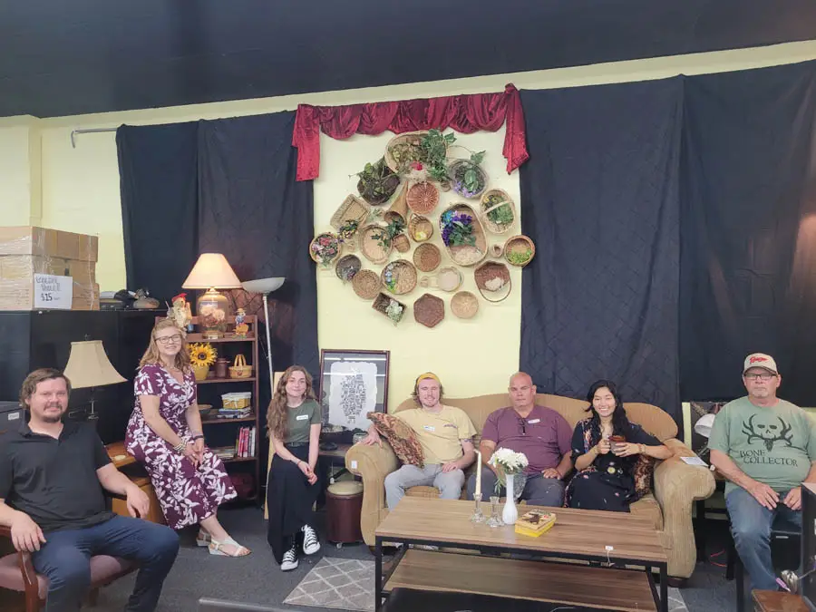 Group of people sitting on couch and chairs posing for photo in thrift store