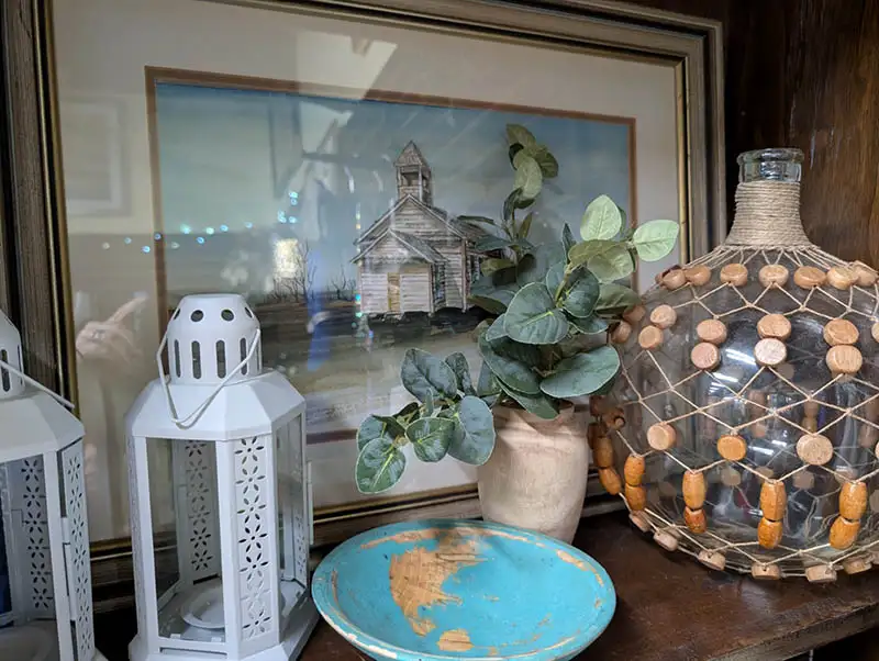 Framed artwork, lamp, vase, fake plant, and plate on shelf