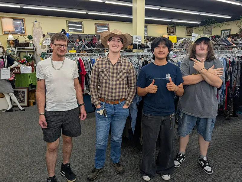 Four people posing for picture in front of clothing racks